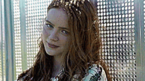 A Woman With Long Red Hair Is Standing In Front Of A Metal Wall And Smiling . GIF
