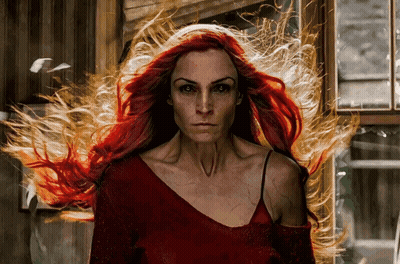 A Woman With Long Red Hair Is Standing In Front Of A Window With Fire Coming Out Of Her Hair GIF