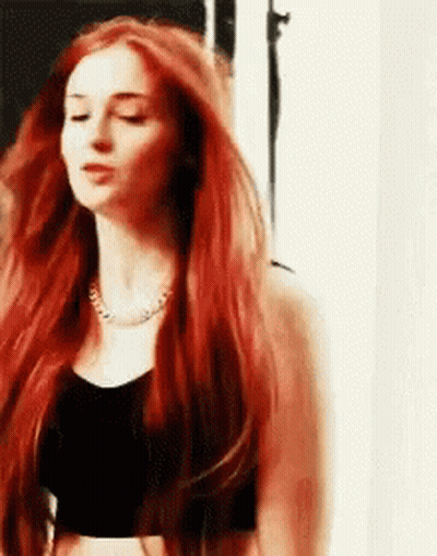 A Woman With Long Red Hair Is Wearing A Black Crop Top . GIF