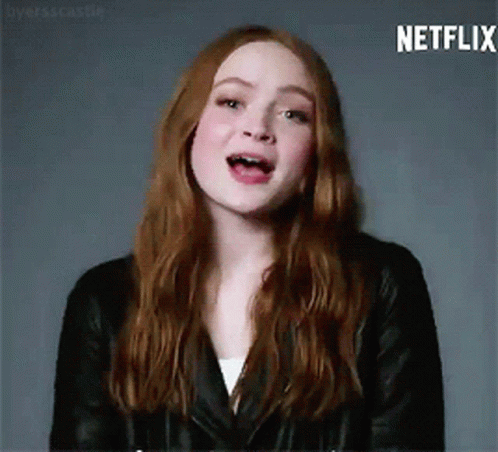 A Woman With Long Red Hair Is Wearing A Black Leather Jacket And A White Shirt . GIF