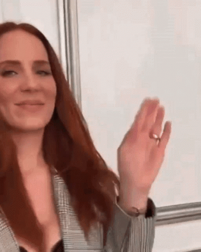 A Woman With Long Red Hair Is Wearing A Ring On Her Finger And Waving Her Hand . GIF