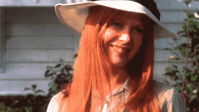A Woman With Long Red Hair Is Wearing A White Hat And Smiling GIF