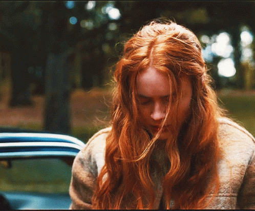 A Woman With Long Red Hair Looks Down In Front Of A Car GIF