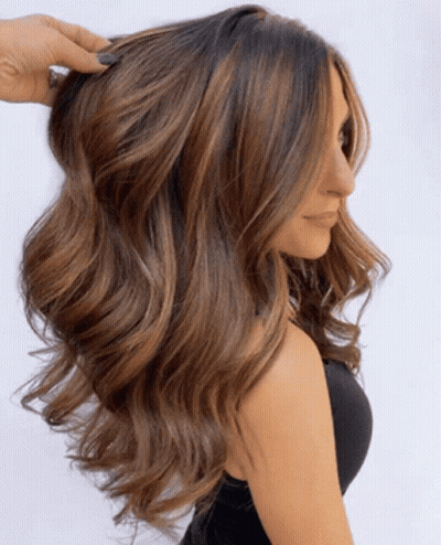 A Woman With Long Wavy Brown Hair Is Wearing A Black Top GIF