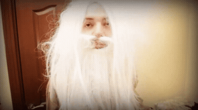 A Woman With Long White Hair And A Beard Looks At The Camera GIF