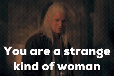 A Woman With Long White Hair Is Standing In A Dark Room With The Words `` You Are A Strange Kind Of Woman '' Above Her . GIF