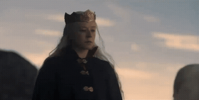 A Woman With Long White Hair Is Wearing A Crown And A Black Coat . GIF