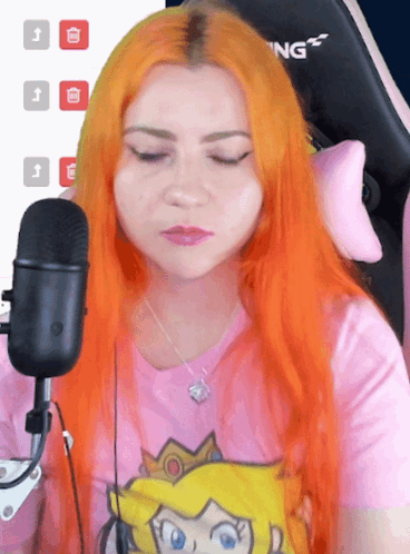 A Woman With Orange Hair Is Sitting In Front Of A Microphone Wearing A Pink Shirt That Says Princess Peach GIF