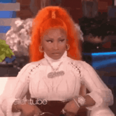 A Woman With Orange Hair Is Sitting On A Couch Wearing A White Shirt . GIF