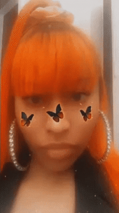 A Woman With Orange Hair Is Wearing Hoop Earrings And Has Three Butterflies On Her Face . GIF