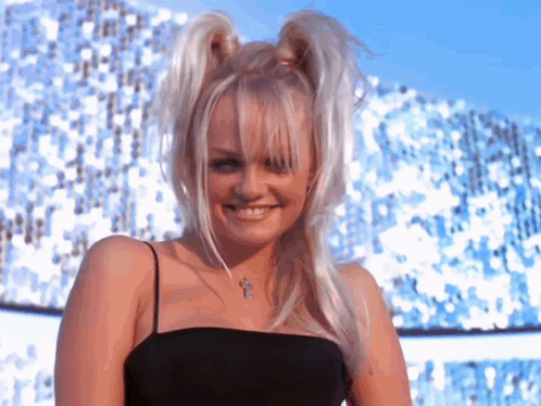 A Woman With Pigtails And A Cross Necklace Is Smiling For The Camera GIF