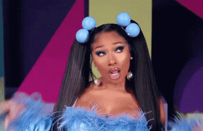 A Woman With Pigtails And Blue Balls In Her Hair Is Wearing A Blue Feathered Top And Earrings . GIF