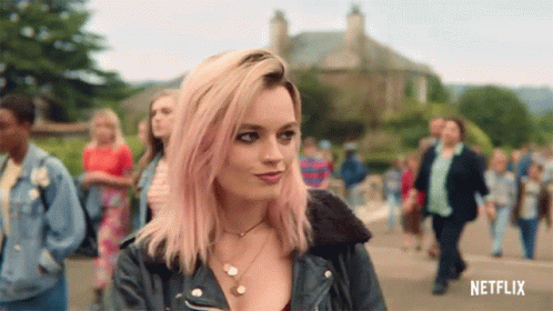 A Woman With Pink Hair And A Leather Jacket Is Standing In Front Of A Crowd . GIF