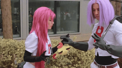 A Woman With Pink Hair And A Man With Purple Hair Are Holding A Toy GIF