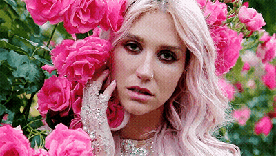 A Woman With Pink Hair And Gloves Is Surrounded By Pink Roses In A Garden . GIF