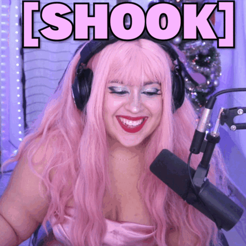 A Woman With Pink Hair And Headphones Is Smiling In Front Of A Microphone With The Words Shook Above Her GIF