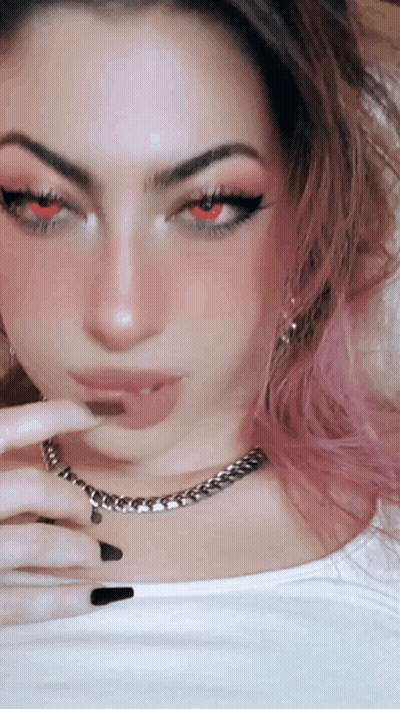A Woman With Pink Hair And Red Eyes Is Wearing A White Shirt And A Chain Around Her Neck . GIF