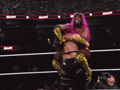 A Woman With Pink Hair Is Being Lifted In A Wrestling Ring By Another Woman GIF