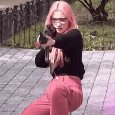 A Woman With Pink Hair Is Holding A Gun In Her Hand While Wearing Safety Glasses . GIF