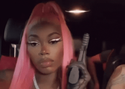 A Woman With Pink Hair Is Holding A Gun While Sitting In A Car . GIF