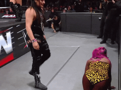 A Woman With Pink Hair Is Kneeling On The Ground In Front Of A Sign That Says N GIF