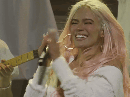 A Woman With Pink Hair Is Singing Into A Microphone And Smiling GIF