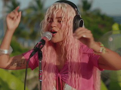 A Woman With Pink Hair Is Singing Into A Microphone And Wearing Headphones GIF