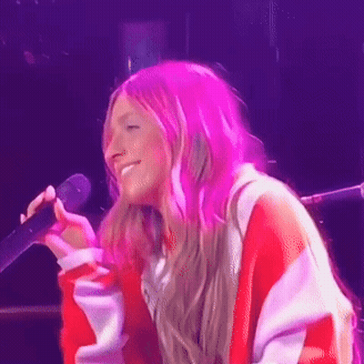 A Woman With Pink Hair Is Singing Into A Microphone On A Stage GIF