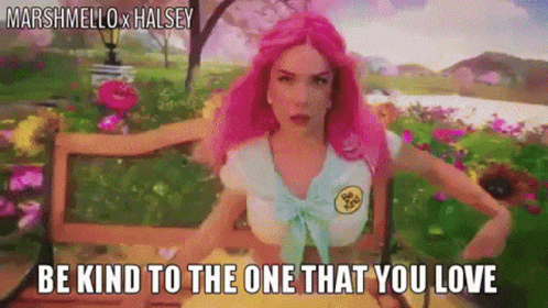 A Woman With Pink Hair Is Sitting On A Bench With Flowers In The Background . GIF
