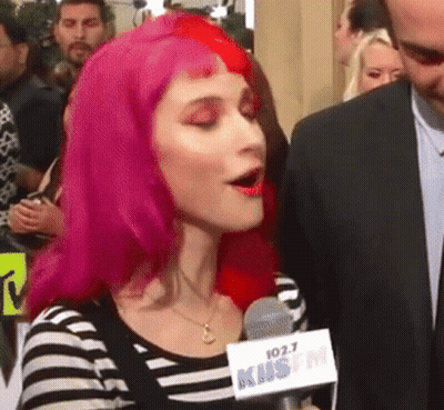 A Woman With Pink Hair Is Speaking Into A Microphone That Says 102.7 Kms Fm GIF