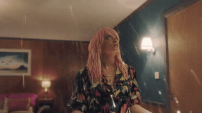 A Woman With Pink Hair Is Standing In A Room In The Rain GIF