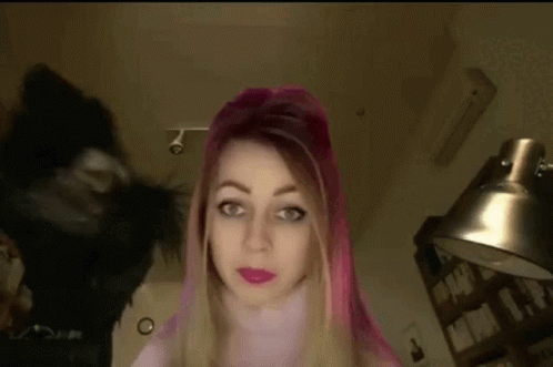 A Woman With Pink Hair Is Standing In Front Of A Lamp And A Black Cat . GIF