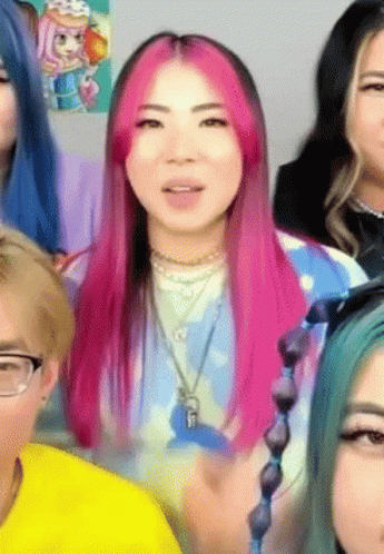 A Woman With Pink Hair Is Surrounded By Other People . GIF