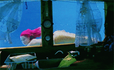 A Woman With Pink Hair Is Swimming Underwater In A Tank GIF