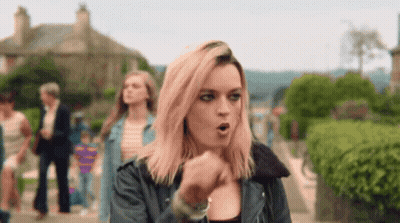 A Woman With Pink Hair Is Walking Down A Street With Her Mouth Open . GIF