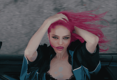 A Woman With Pink Hair Is Wearing A Blue Jacket And Black Bra GIF