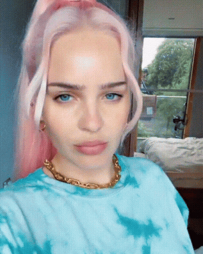 A Woman With Pink Hair Is Wearing A Blue Tie Dye Shirt And A Gold Chain Around Her Neck GIF