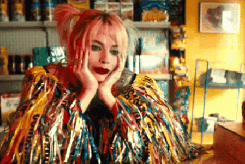 A Woman With Pink Hair Is Wearing A Colorful Feathered Coat GIF