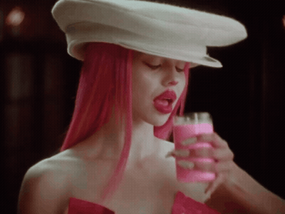 A Woman With Pink Hair Is Wearing A White Hat And Holding A Pink Drink . GIF