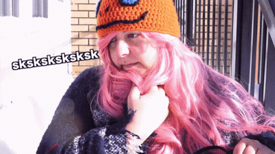 A Woman With Pink Hair Is Wearing An Orange Crocheted Hat GIF
