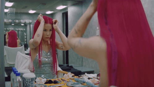 A Woman With Pink Hair Looks At Herself In The Mirror GIF
