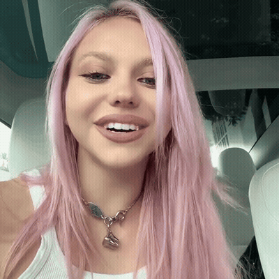 A Woman With Pink Hair Wearing A White Tank Top And A Necklace GIF