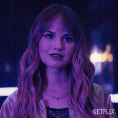 A Woman With Purple Hair And A Necklace Is Standing In Front Of A Purple Light . GIF