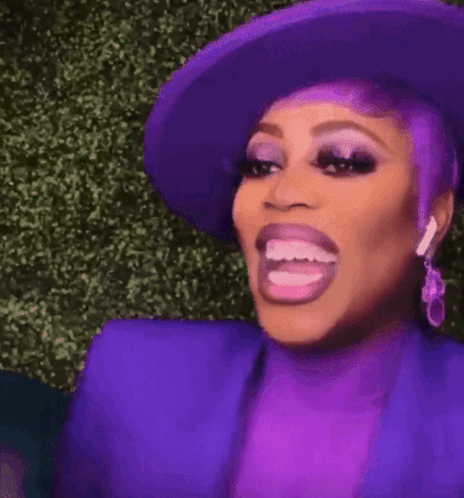 A Woman With Purple Hair And A Purple Hat Is Making A Funny Face With Her Mouth Open . GIF