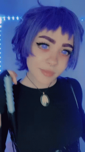 A Woman With Purple Hair And Blue Eyes Is Wearing A Black Top And A Necklace GIF