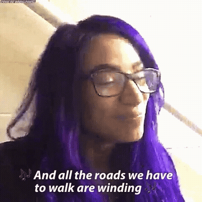 A Woman With Purple Hair And Glasses Is Saying `` And All The Roads We Have To Walk Are Winding `` . GIF