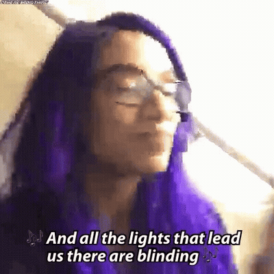 A Woman With Purple Hair And Glasses Is Singing A Song . GIF