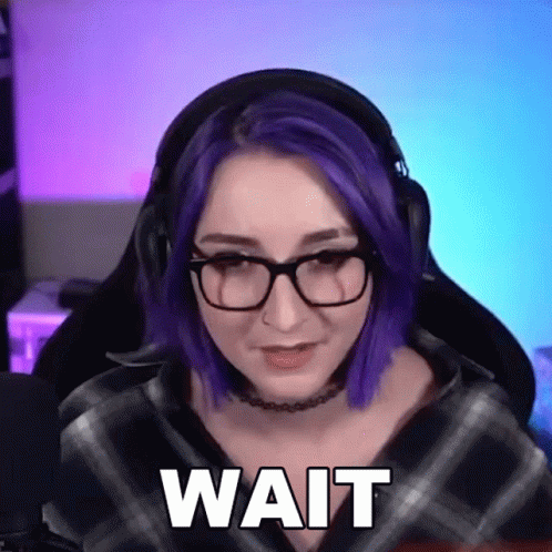 A Woman With Purple Hair And Glasses Is Wearing Headphones And Has The Word Wait On Her Face . GIF