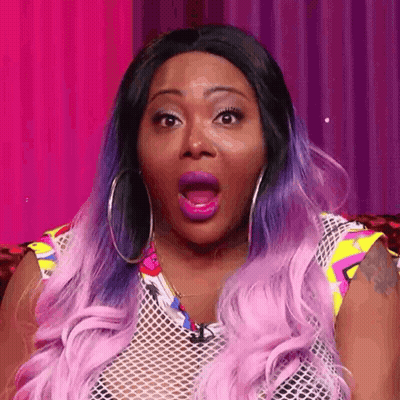 A Woman With Purple Hair And Hoop Earrings Is Making A Surprised Face With Her Mouth Open . GIF