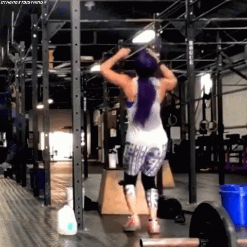 A Woman With Purple Hair Is Doing Pull Ups In A Gym GIF